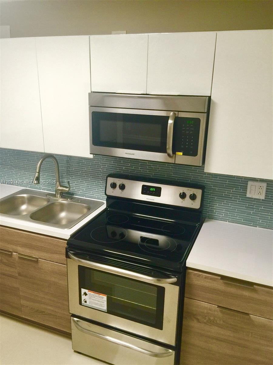 A kitchen features white upper cabinets, wood-grain lower cabinets, stainless steel appliances, and blue tile — NORTH MIAMI, FL