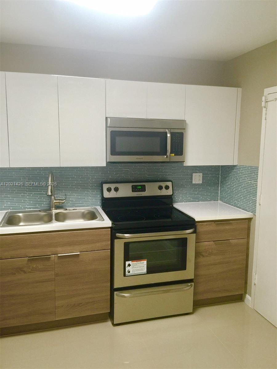 A kitchen features white upper cabinets, wood-tone lower cabinets, stainless steel appliances, and blue tile — NORTH MIAMI, FL