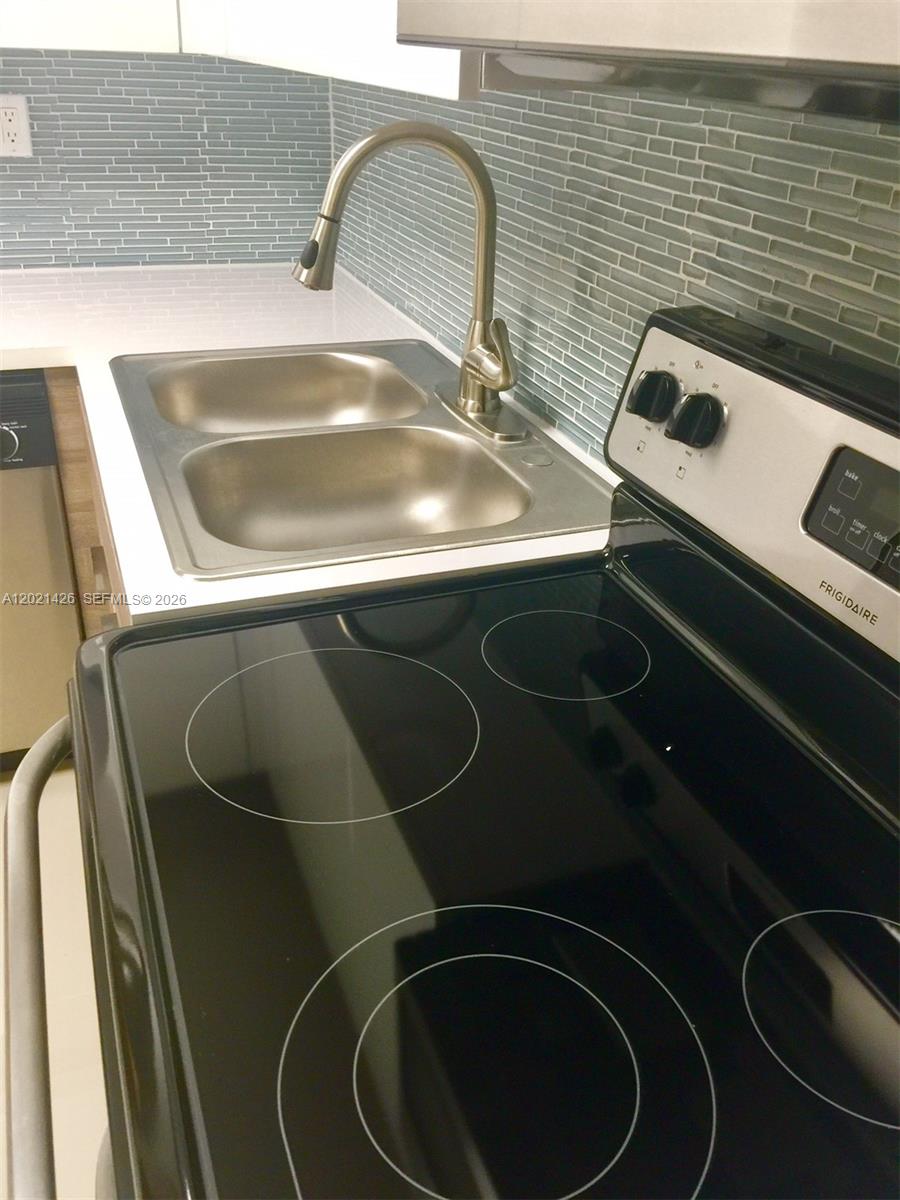 A kitchen features a stainless steel sink, a faucet, and a black glass-top stove — NORTH MIAMI, FL