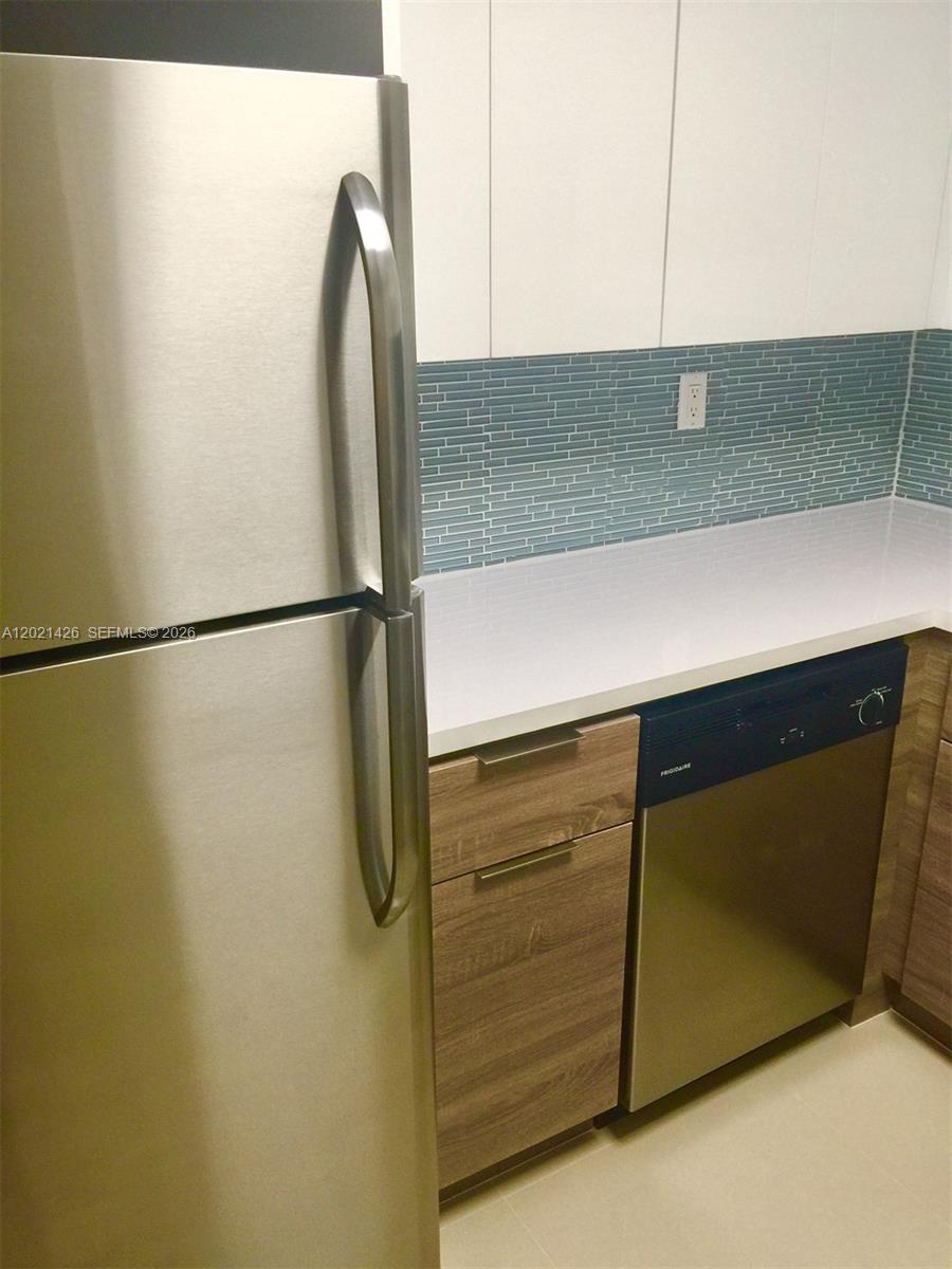 A kitchen features a stainless steel refrigerator, a dishwasher, wood-grain cabinets, and a blue backsplash — NORTH MIAMI, FL