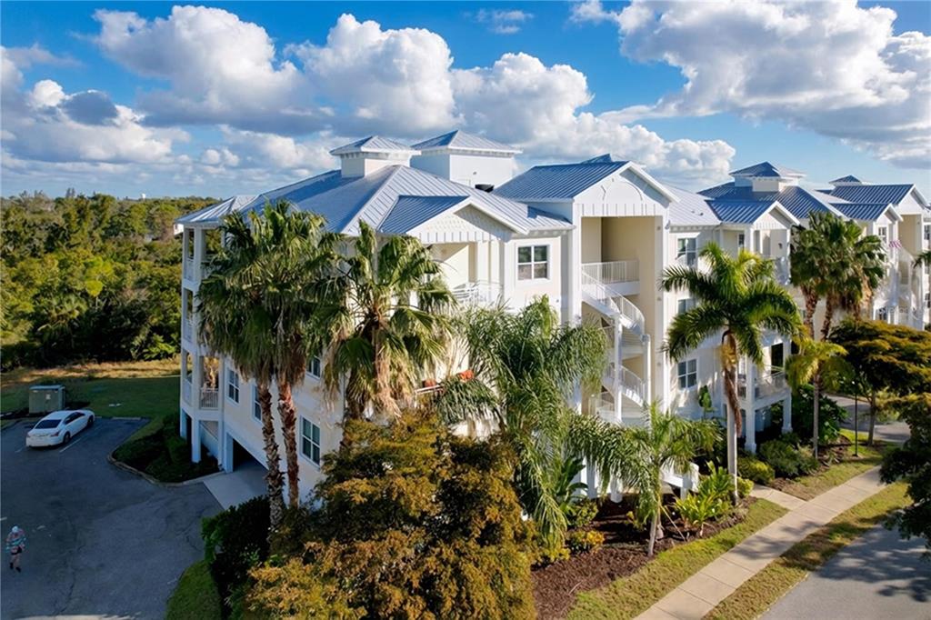 An exterior view of a multi-story residential building with a metal roof and palm trees — 7730 34TH AVE W UNIT 303, BRADENTON, FL