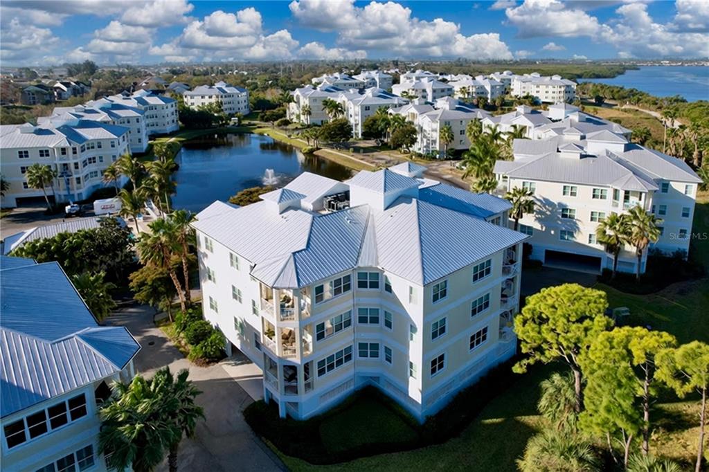 An aerial view of multi-story residential buildings with metal roofs surrounding a small lake — 7730 34TH AVE W UNIT 303, BRADENTON, FL