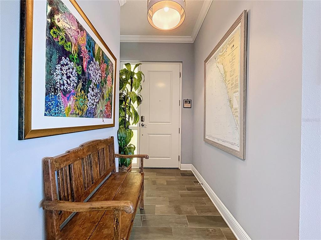 A hallway features a wooden bench, two framed wall artworks, and a white front door — 7730 34TH AVE W UNIT 303, BRADENTON, FL