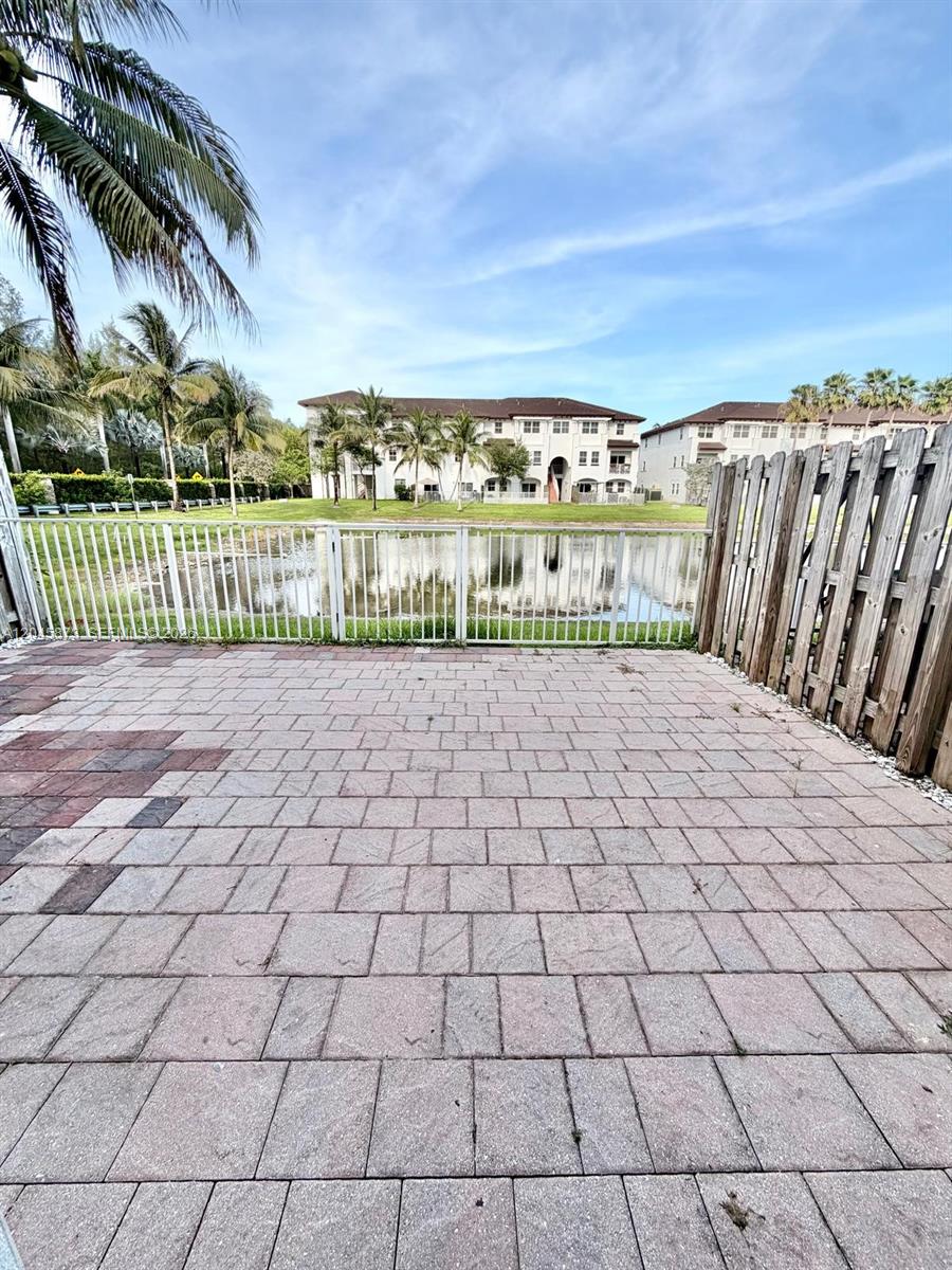 A paved patio overlooks a small lake with residential buildings in the background — 8965 NW 98th Ave, Doral FL 33178, DORAL, FL