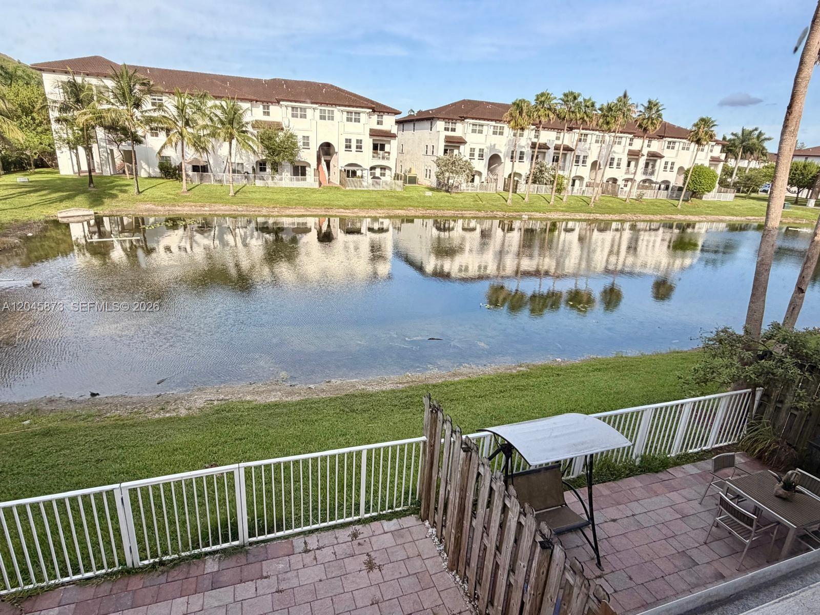 A patio with a swing and table overlooks a pond and multi-story apartment buildings — 8965 NW 98th Ave, Doral FL 33178, DORAL, FL