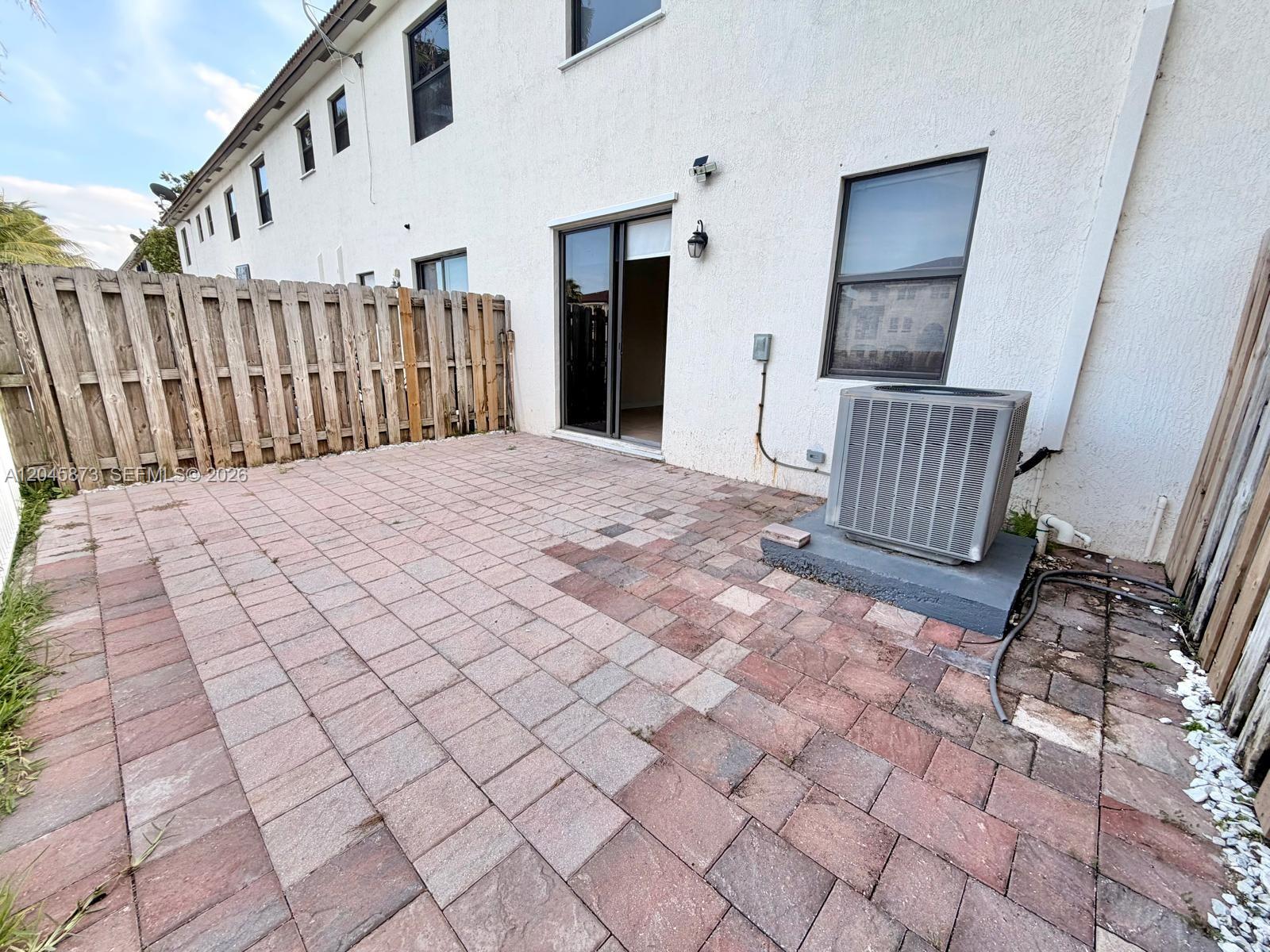 A paved patio area features a sliding glass door, a window, and an outdoor AC unit — 8965 NW 98th Ave, Doral FL 33178, DORAL, FL