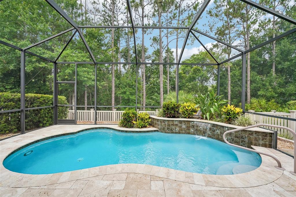 A screened-in swimming pool with a stone waterfall feature and travertine deck — 2919 DEVONOAK BOULEVARD, LAND O LAKES, FL
