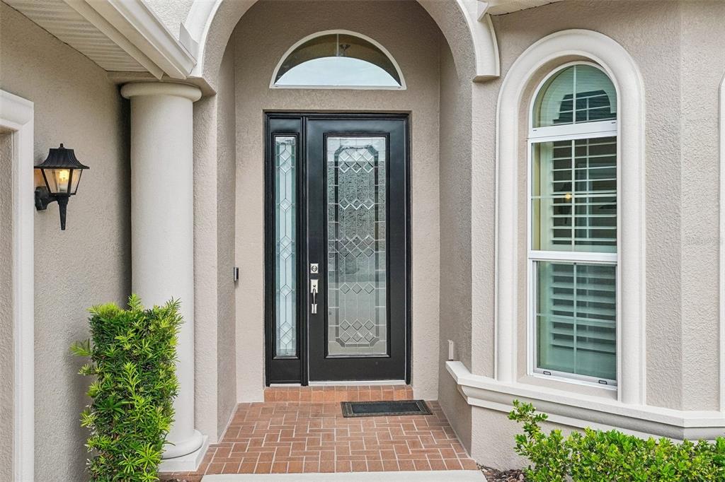 A black front door with glass panels sits under an arched entryway with a window — 2919 DEVONOAK BOULEVARD, LAND O LAKES, FL