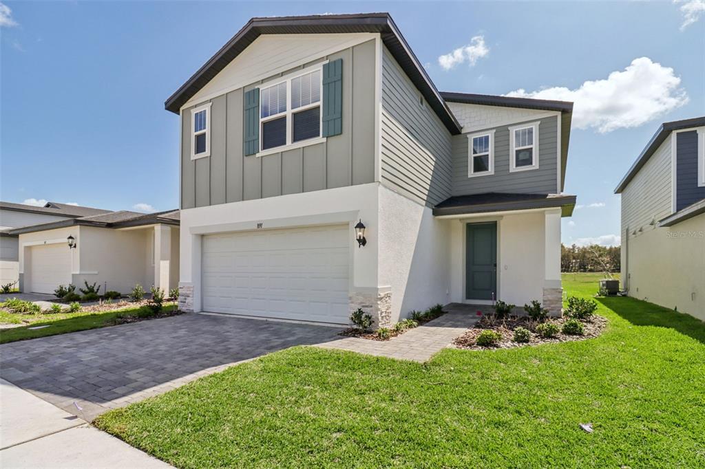 A two-story house with a white stucco garage, gray siding, and a paved driveway — 891 SUNSHOWER DRIVE, LADY LAKE, FL