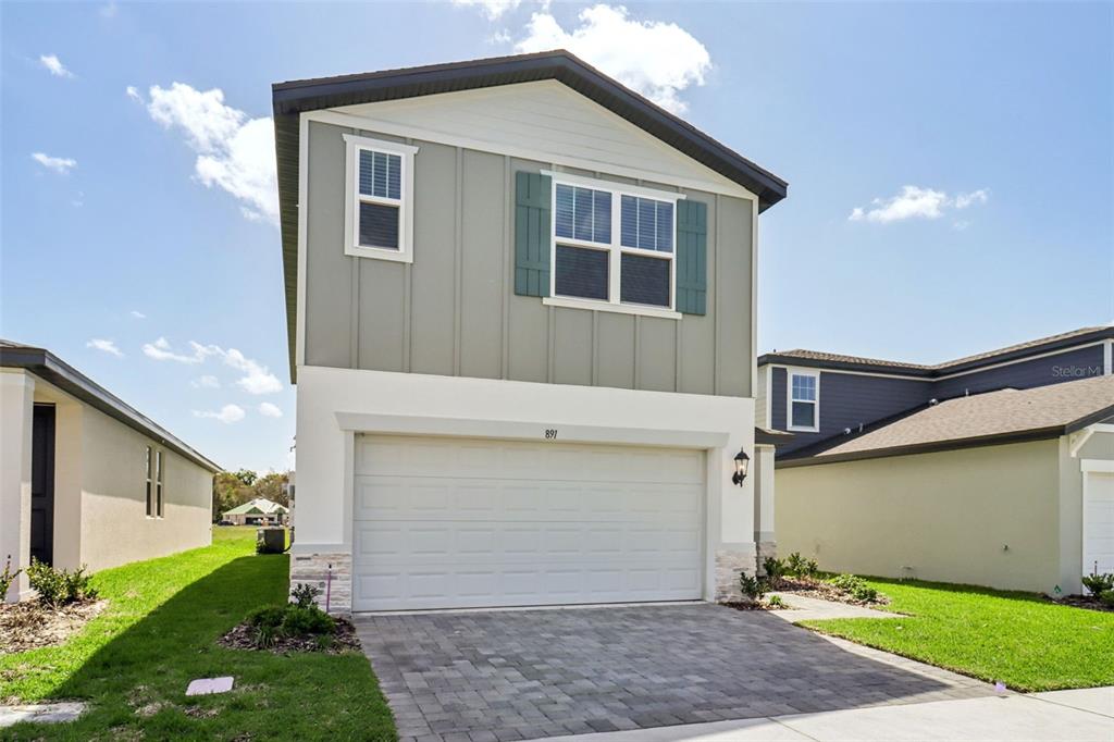 A two-story house with a white garage, green vertical siding, and a paved driveway — 891 SUNSHOWER DRIVE, LADY LAKE, FL