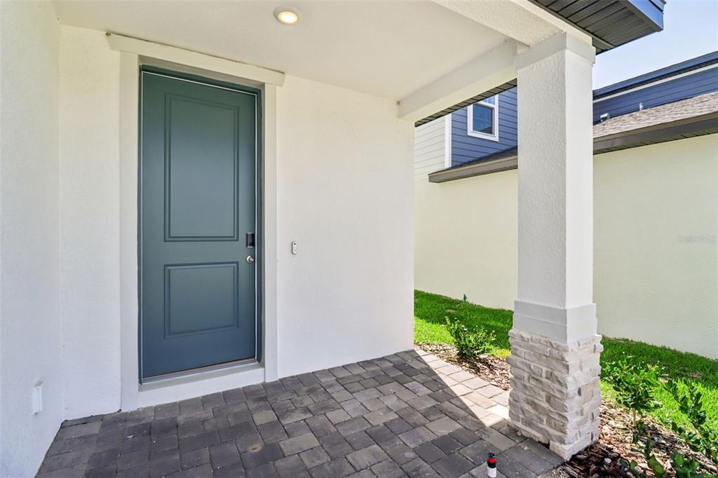 A covered front porch features a teal door, stone-based pillar, and gray paver flooring — 891 SUNSHOWER DRIVE, LADY LAKE, FL