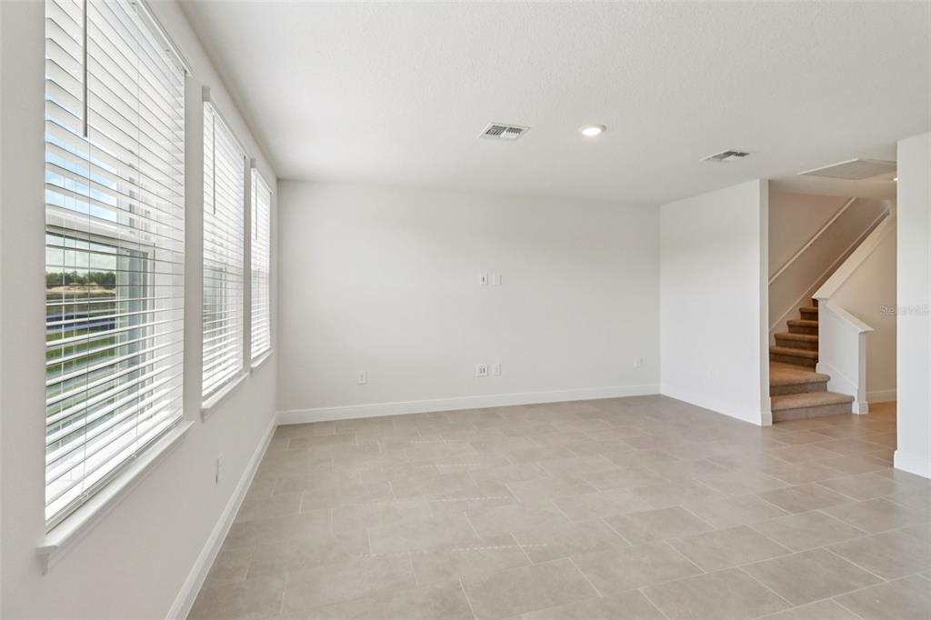 An empty room with light-colored tile flooring, white walls, large windows, and a staircase — 891 SUNSHOWER DRIVE, LADY LAKE, FL