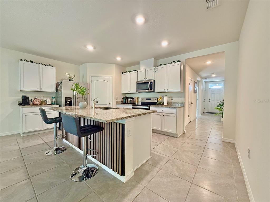 A kitchen with white cabinets, granite countertops, a center island with bar stools, and tile flooring — 2033 E GLORIA DRIVE, DELTONA, FL
