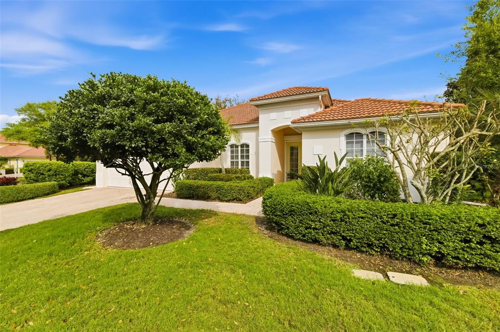 A single-story house with a tiled roof, manicured hedges, and a large tree in front — 7418 MONTE VERDE, SARASOTA, FL