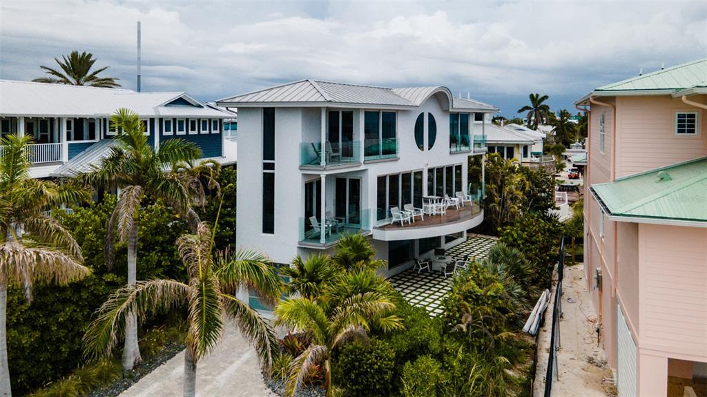An elevated white house with a curved balcony sits between two other coastal homes — 107 ELM AVENUE, ANNA MARIA, FL