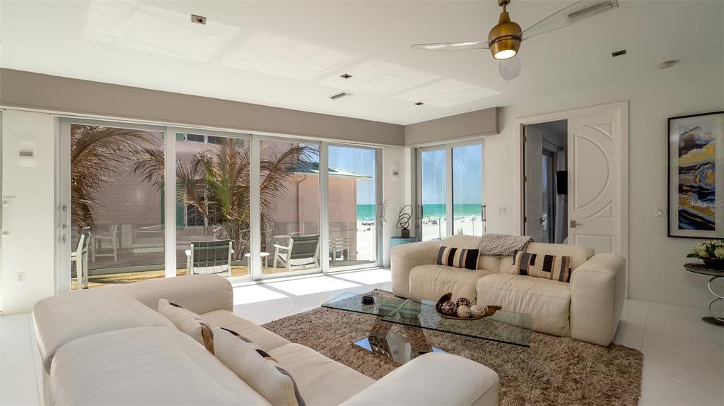 A bright living room with white leather sofas, a glass coffee table, and beach views — 107 ELM AVENUE, ANNA MARIA, FL