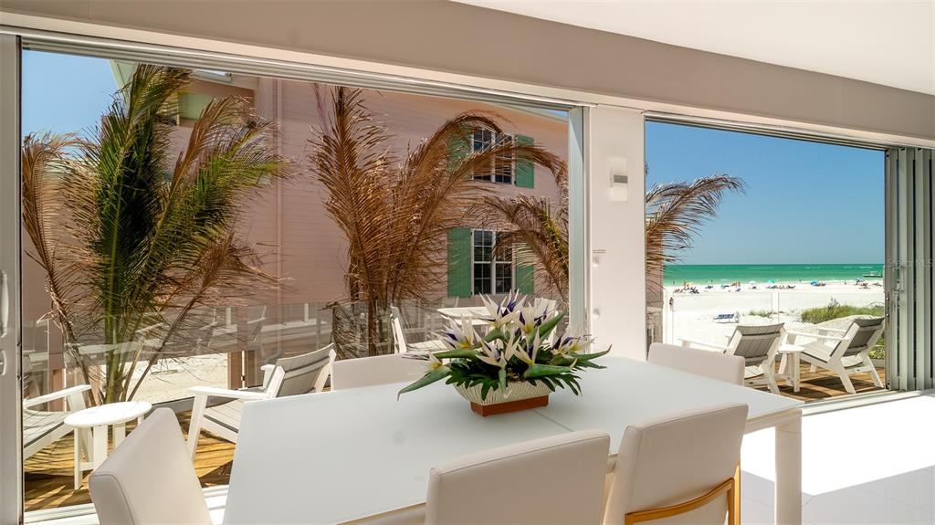 A dining room with a white table and chairs overlooks a beach through large windows — 107 ELM AVENUE, ANNA MARIA, FL