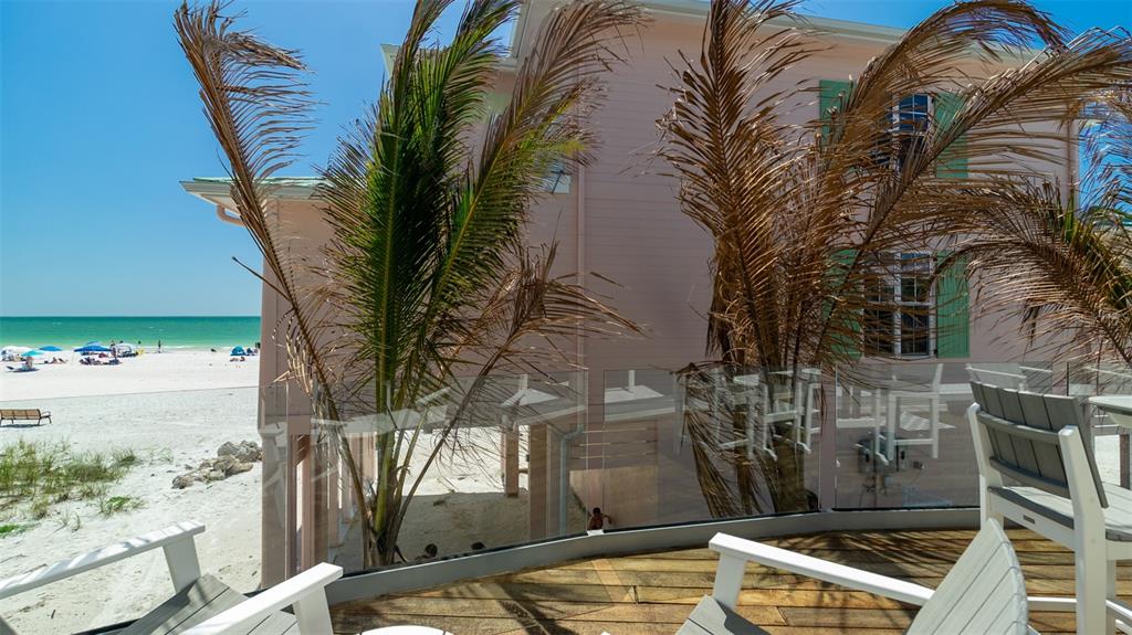 A wooden deck with chairs overlooks a sandy beach and the ocean from a house — 107 ELM AVENUE, ANNA MARIA, FL