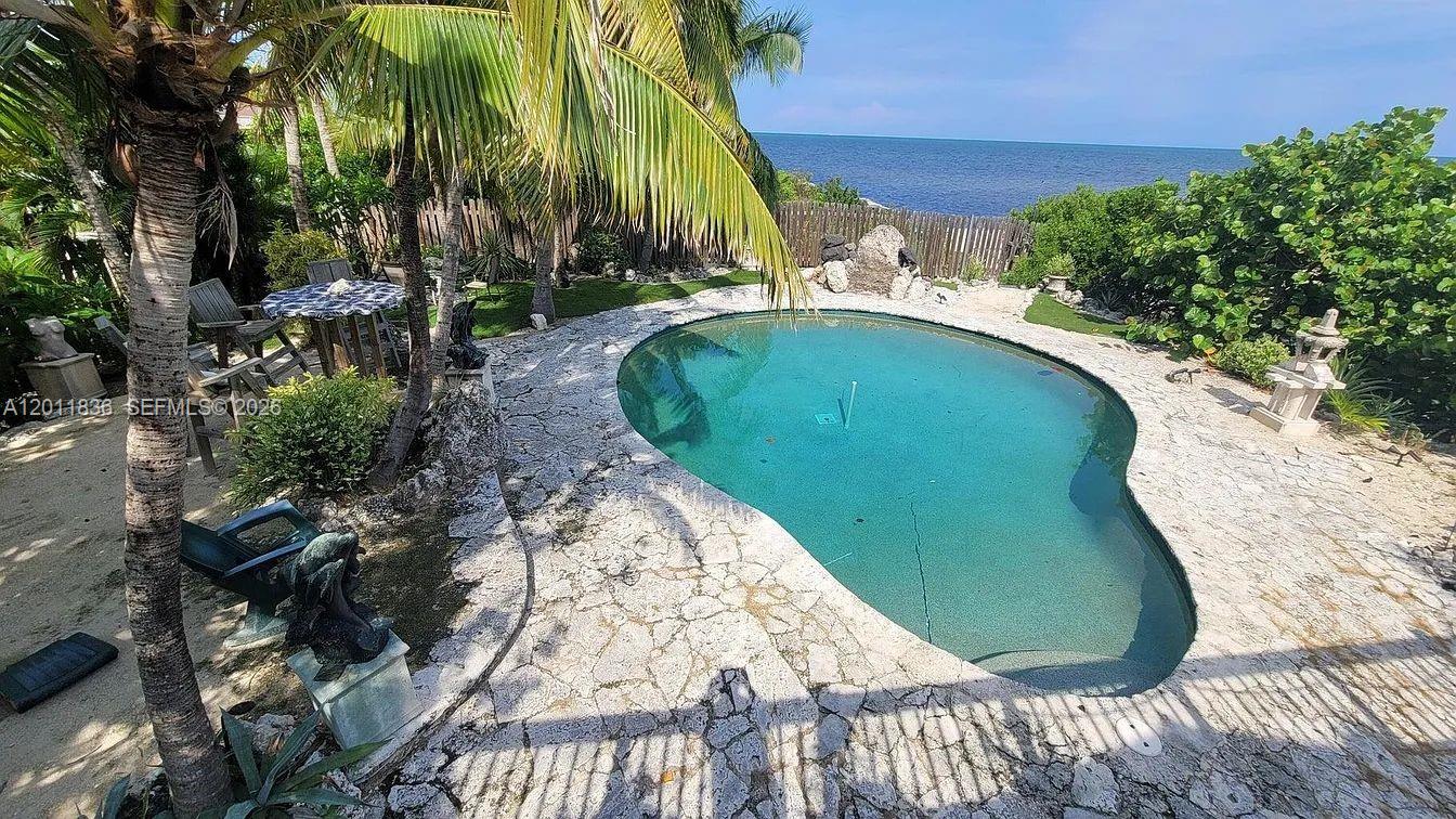 An outdoor swimming pool with a stone deck sits near palm trees and the ocean — 167 Valois Blvd, Key Largo FL 33037, KEY LARGO, FL