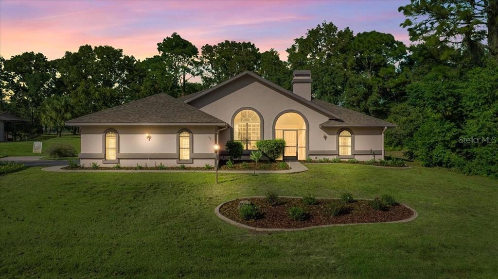A single-story house with a stucco exterior, arched windows, and a front lawn at dusk — 631 E LIBERTY STREET, HERNANDO, FL