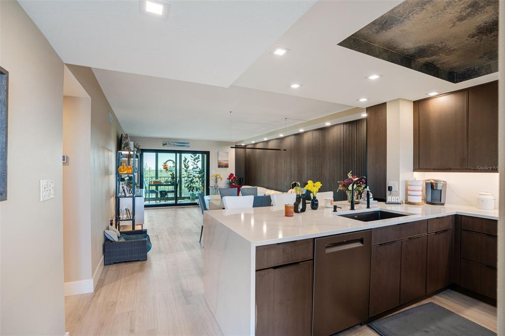 A modern kitchen with dark wood cabinets and a white waterfall island overlooks a living area — 9397 MIDNIGHT PASS ROAD UNIT 905, SARASOTA, FL