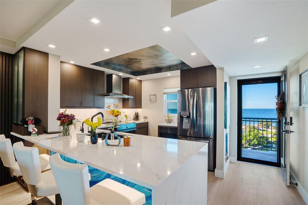 A modern kitchen features a white quartz island, dark cabinetry, and a balcony with ocean views — 9397 MIDNIGHT PASS ROAD UNIT 905, SARASOTA, FL