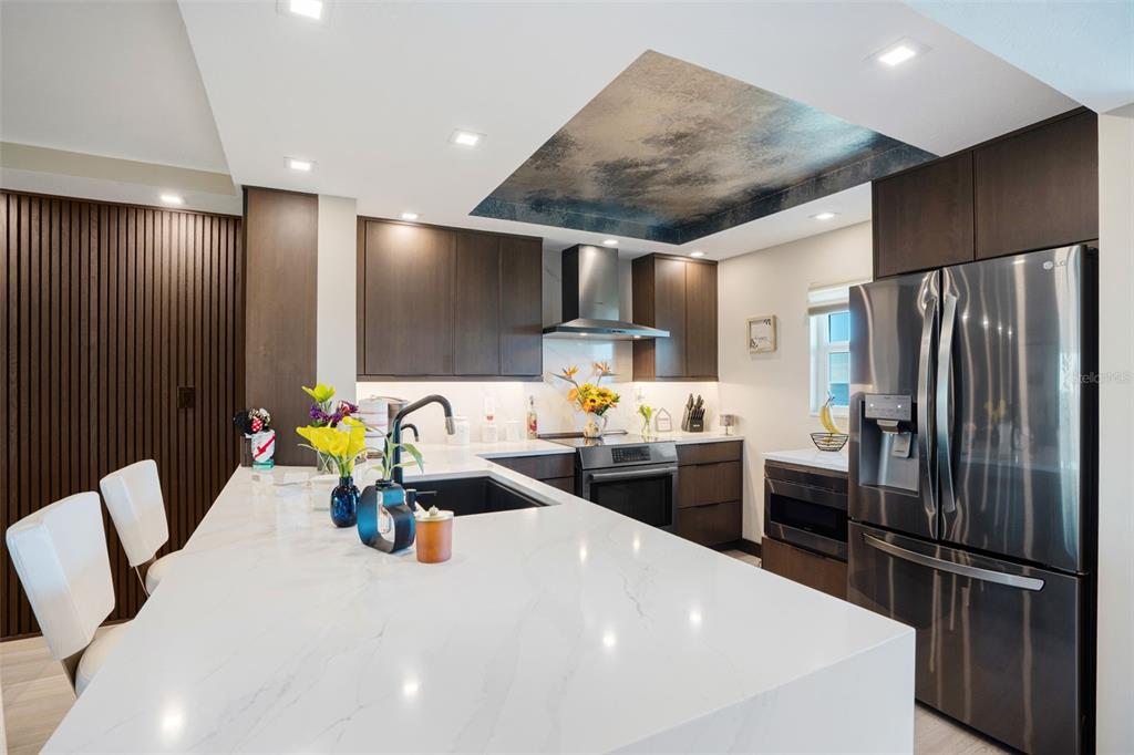 A modern kitchen features dark wood cabinetry, a white quartz island, and a textured ceiling — 9397 MIDNIGHT PASS ROAD UNIT 905, SARASOTA, FL