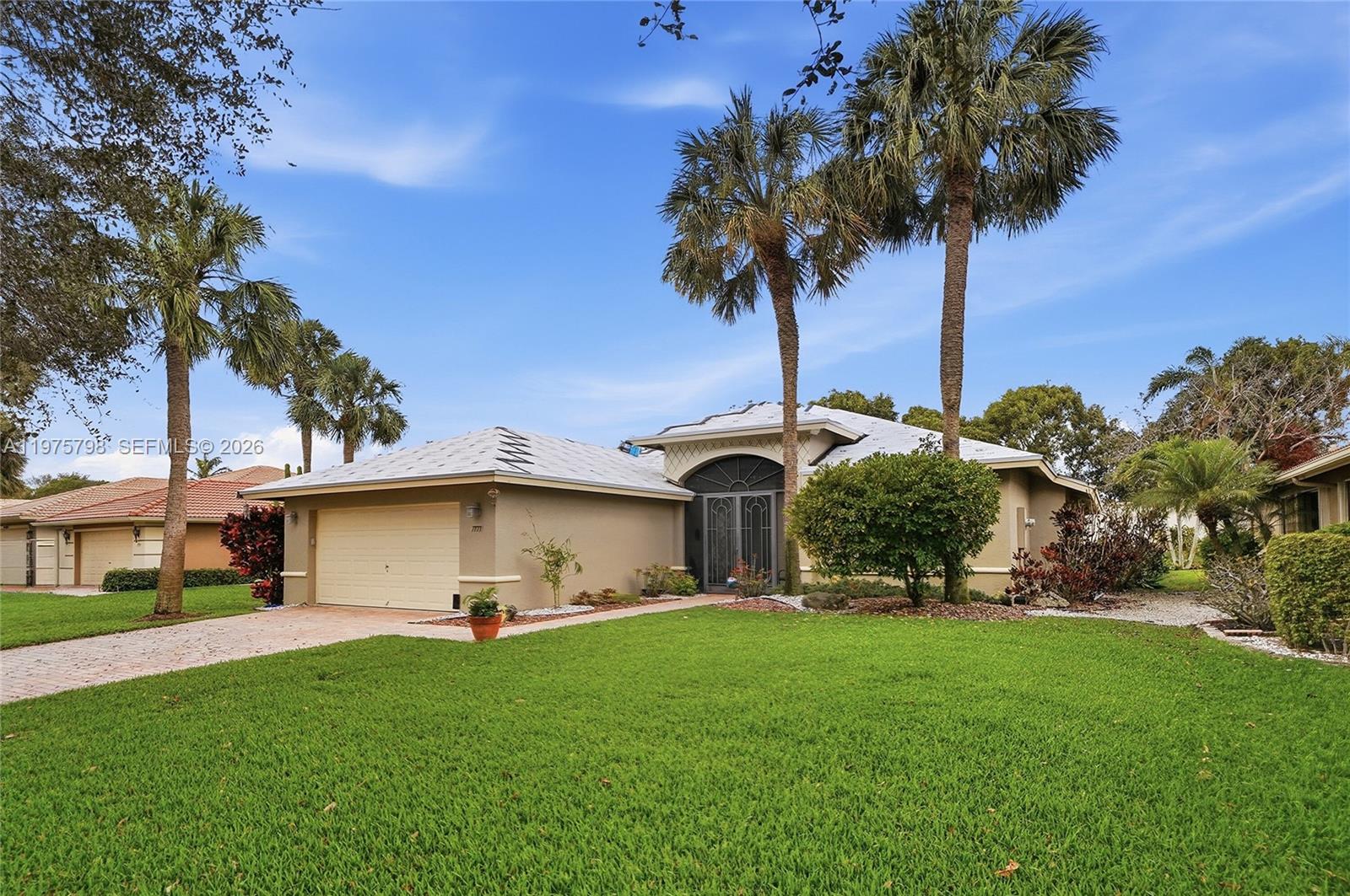 A beige house exterior features a garage, a brick paver walkway, and a screened entryway — 7771 Via Grande, Boynton Beach FL 33437, BOYNTON BEACH, FL
