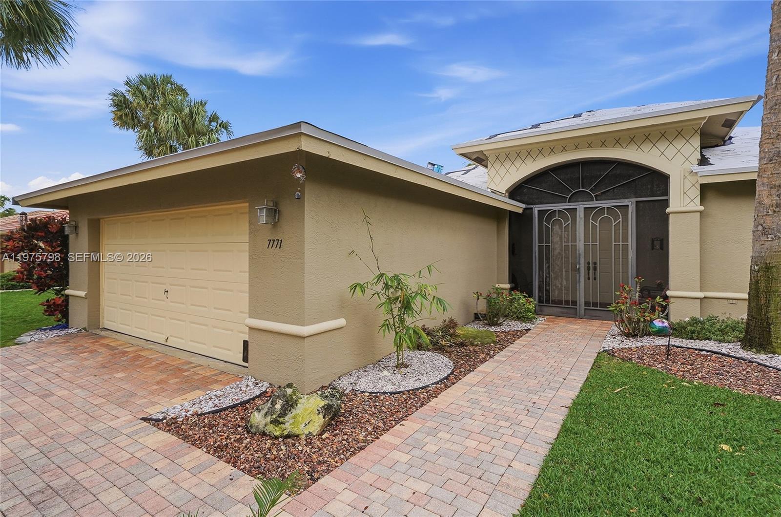 The exterior of a single-story house features a garage, a paved walkway, and landscaping — 7771 Via Grande, Boynton Beach FL 33437, BOYNTON BEACH, FL
