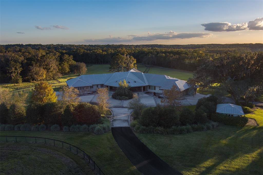 An aerial view shows a sprawling single-story house with a metal roof and circular driveway — 9504 NW HWY 320, MICANOPY, FL