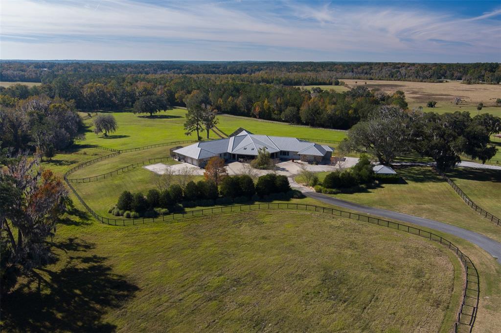 An aerial view of a large house with a metal roof surrounded by fenced pastures — 9504 NW HWY 320, MICANOPY, FL
