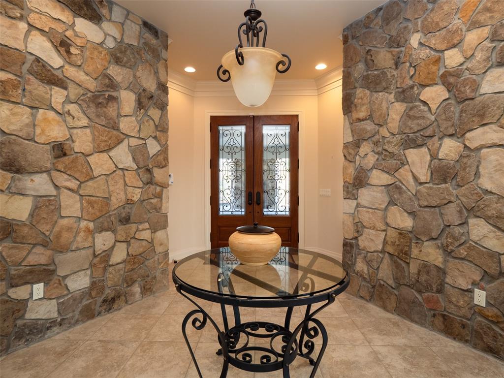 An entryway features stone walls, a glass-topped table, and a decorative chandelier — 9504 NW HWY 320, MICANOPY, FL