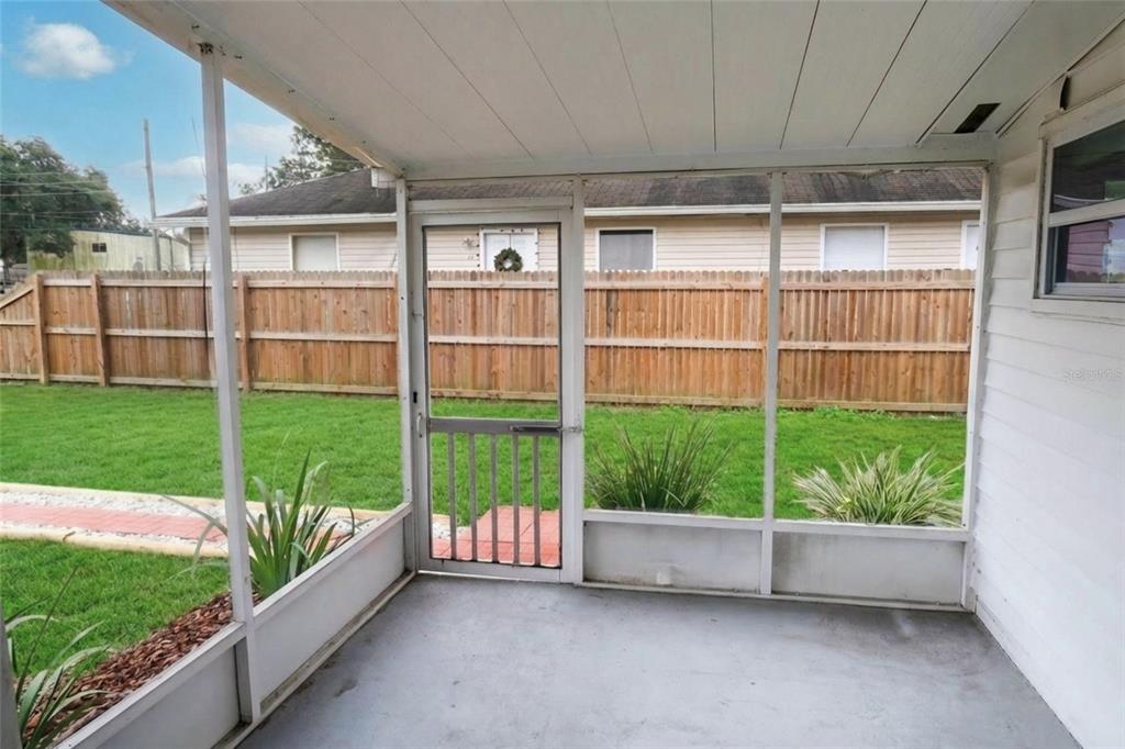 A screened-in porch with a concrete floor overlooks a fenced backyard with a grassy lawn — 4829 6TH STREET, ZEPHYRHILLS, FL