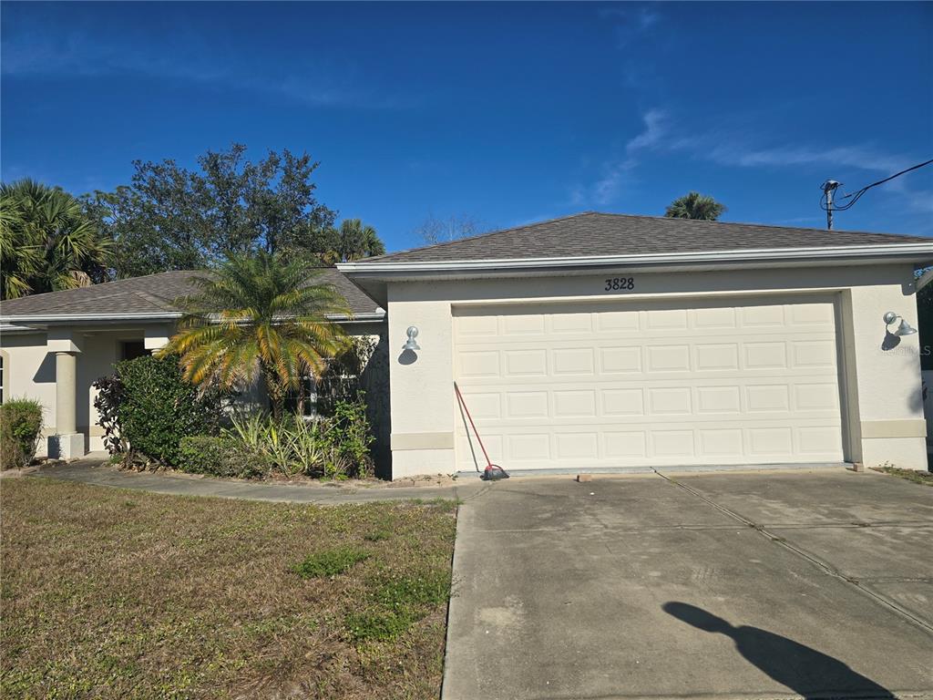 A single-story house with a beige stucco exterior, a two-car garage, and a palm tree — 3828 TRENTON LANE, NORTH PORT, FL