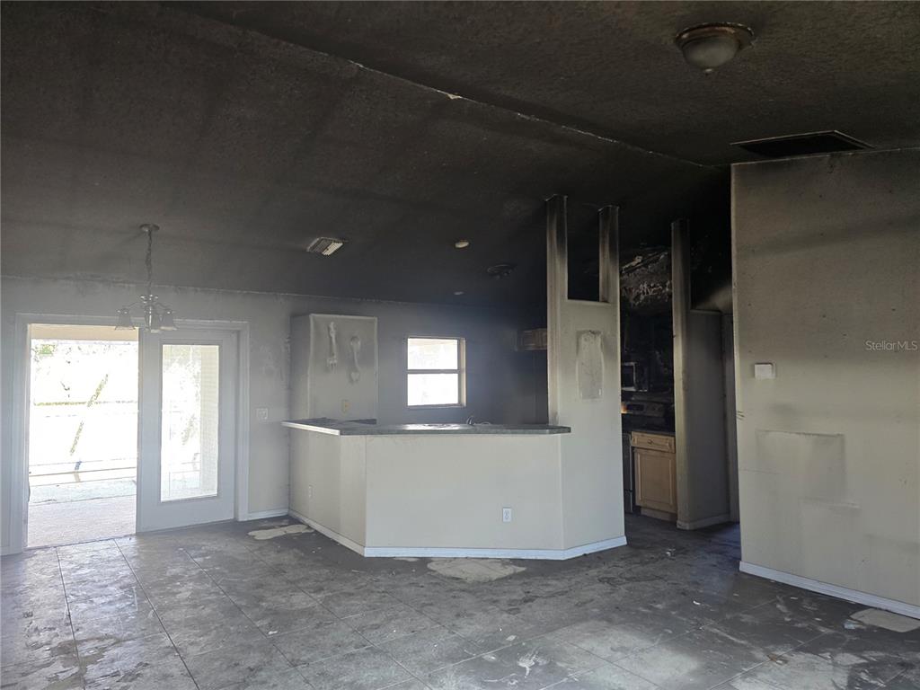 An interior view of a kitchen and living area showing significant fire and smoke damage — 3828 TRENTON LANE, NORTH PORT, FL