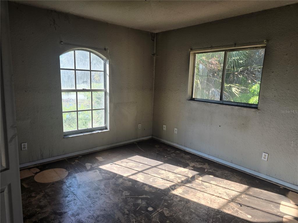 An empty room with dark, worn flooring, two windows, and unfinished walls — 3828 TRENTON LANE, NORTH PORT, FL