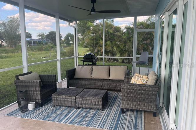 A screened-in patio features wicker furniture, a ceiling fan, and a view of a grassy yard — 118 CADDY ROAD, ROTONDA WEST, FL