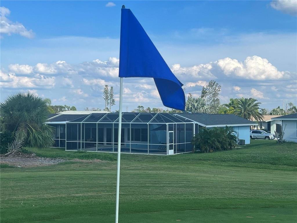 A blue golf flag stands on a green in front of a house with a screened-in pool — 118 CADDY ROAD, ROTONDA WEST, FL