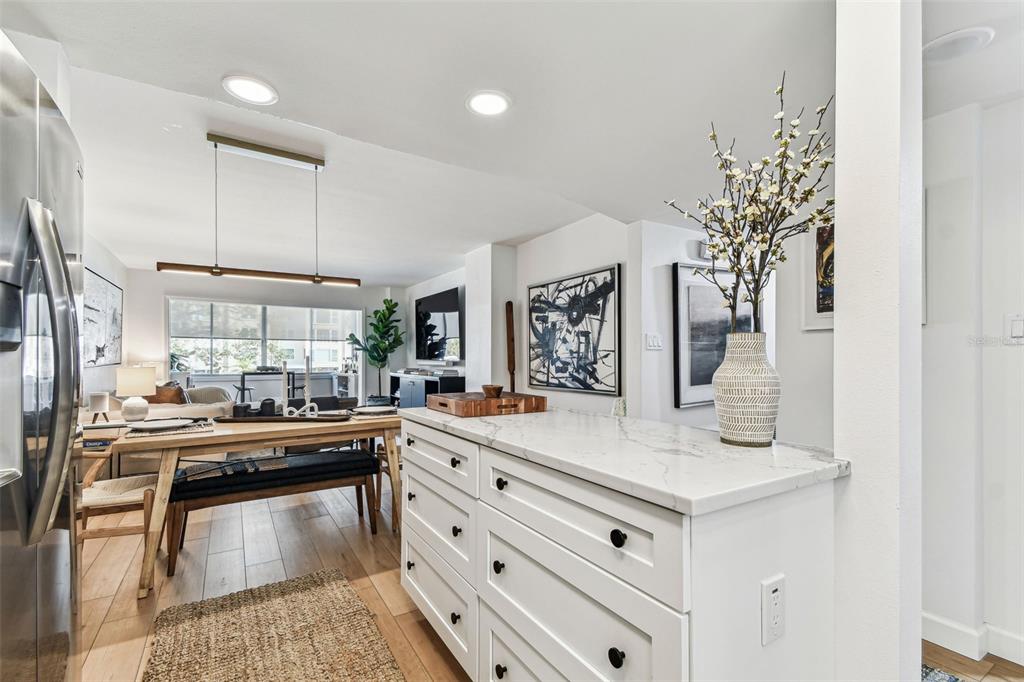 A white kitchen island with a marble countertop sits in front of a dining area — 620 EDGEWATER DRIVE UNIT 204, DUNEDIN, FL