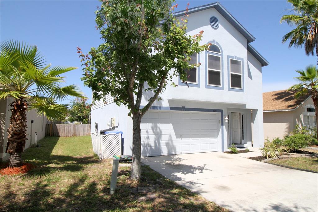 A two-story light blue house with a white garage door and palm trees in front — 10410 OPUS DRIVE, RIVERVIEW, FL