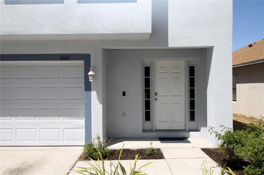 A white front door with sidelights sits next to a garage under a light-colored overhang — 10410 OPUS DRIVE, RIVERVIEW, FL
