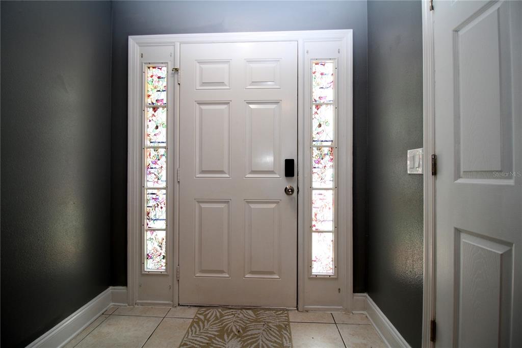 A white front door with stained glass sidelights sits in a tiled entryway with gray walls — 10410 OPUS DRIVE, RIVERVIEW, FL