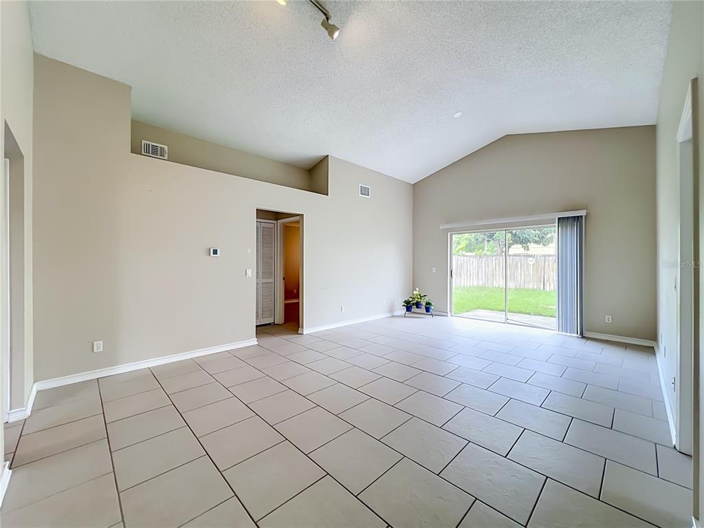 A spacious living room features vaulted ceilings, light-colored tile flooring, and sliding glass patio doors — 930 RIVECON AVENUE, ORLANDO, FL