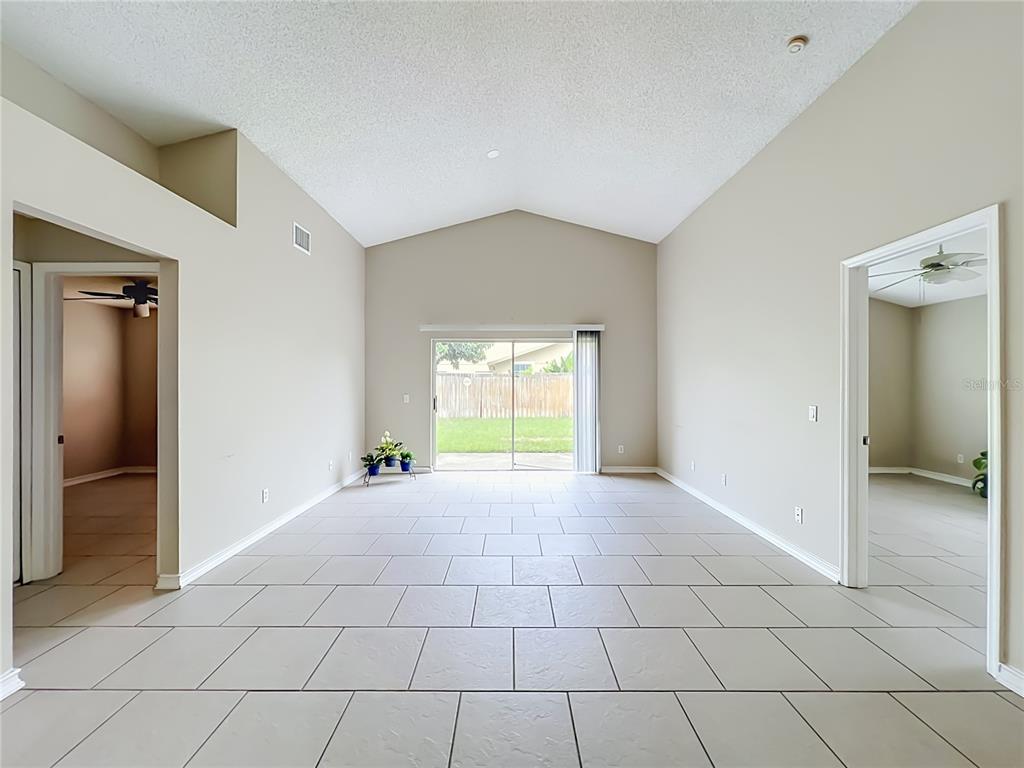 A bright living room with vaulted ceilings, light-colored tile flooring, and sliding glass patio doors — 930 RIVECON AVENUE, ORLANDO, FL