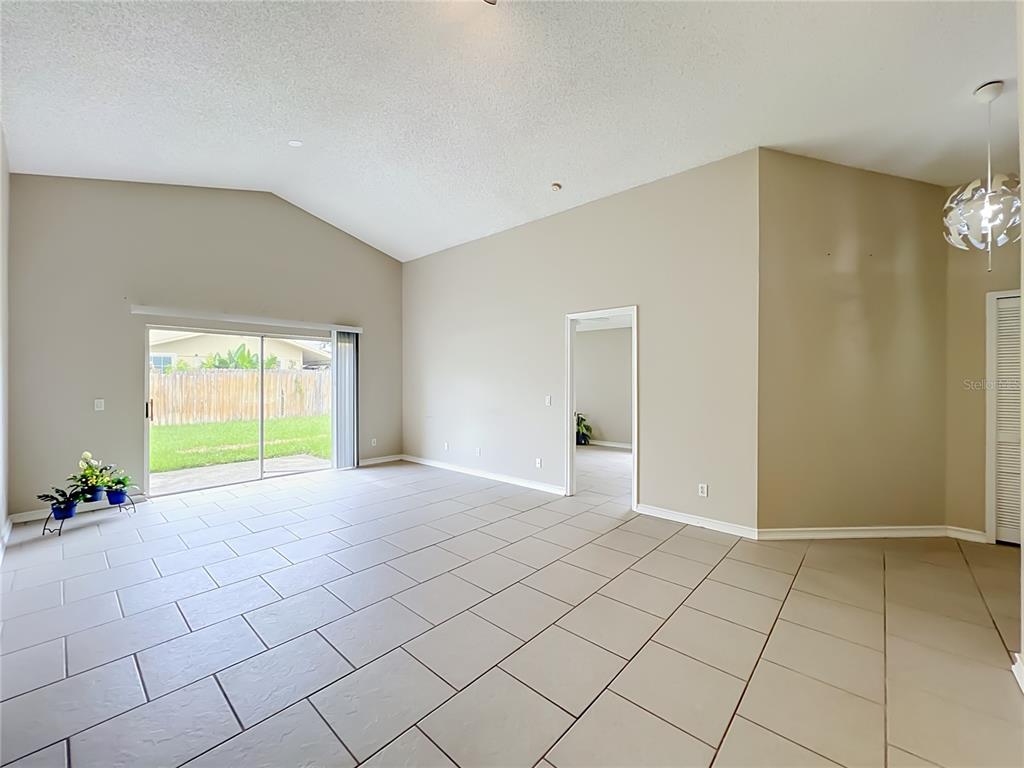 An empty living room with light tile flooring, vaulted ceilings, and sliding glass patio doors — 930 RIVECON AVENUE, ORLANDO, FL