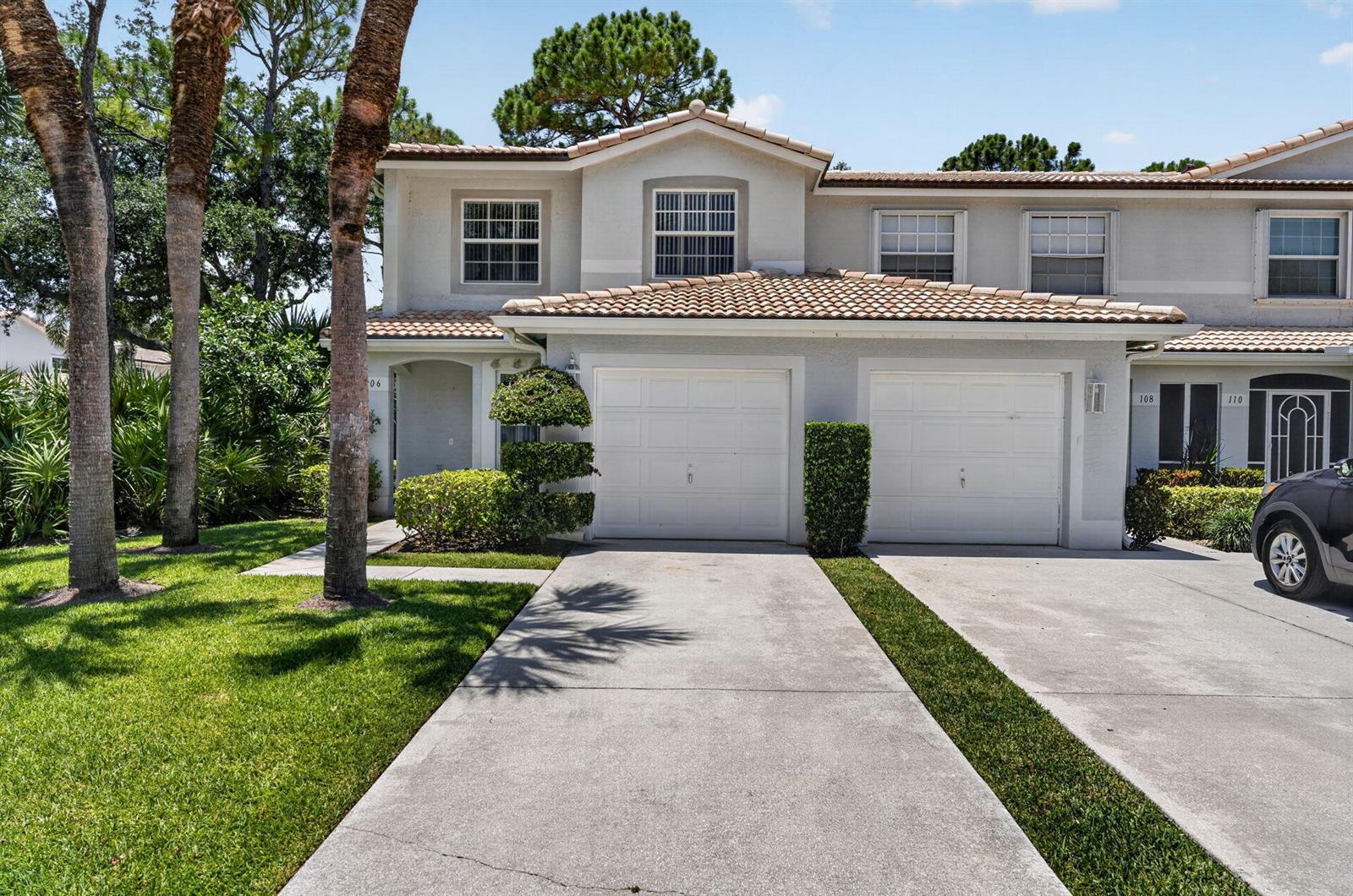 A two-story townhouse with a light-colored stucco exterior, two garage doors, and a tiled roof — 106 Fox Meadow Run, Jupiter FL 33458, JUPITER, FL