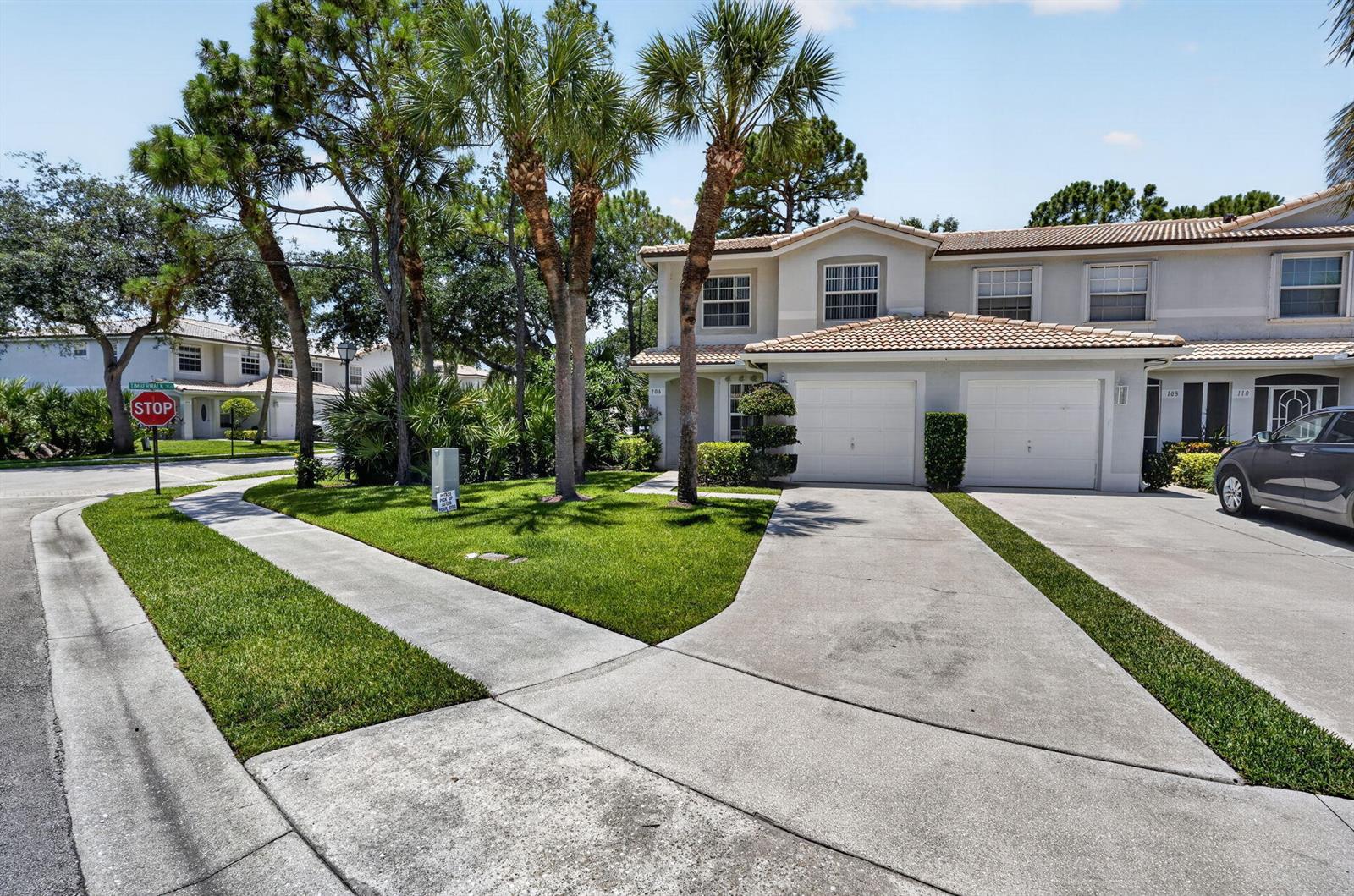 A two-story townhouse with a two-car garage, concrete driveway, and palm trees in front — 106 Fox Meadow Run, Jupiter FL 33458, JUPITER, FL