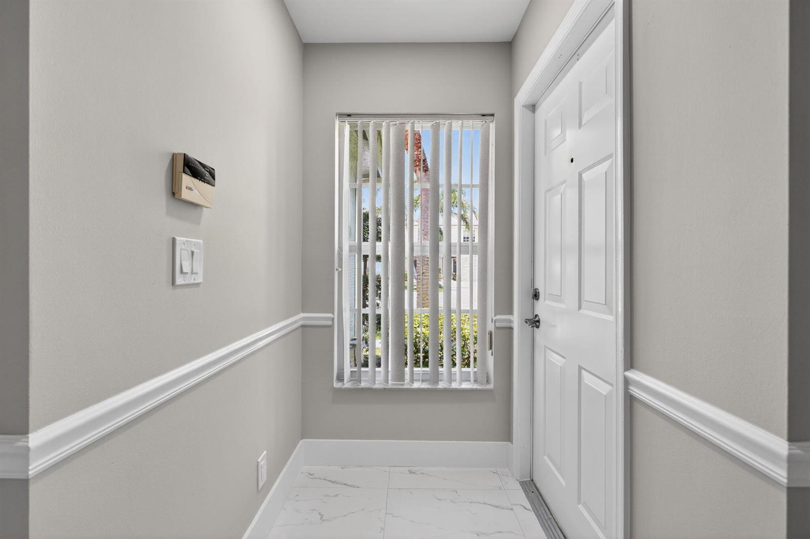 A bright entryway features white tile floors, light gray walls, a window with vertical blinds, and a white door — 106 Fox Meadow Run, Jupiter FL 33458, JUPITER, FL