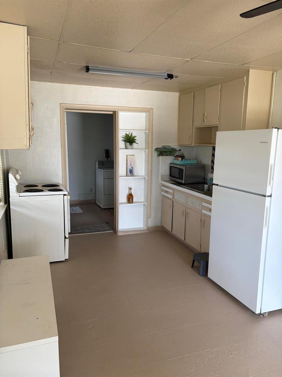 A kitchen features beige cabinets, a white refrigerator, an electric stove, and built-in wall shelving — 198 SE 4th Street, Delray Beach FL 33483, DELRAY BEACH, FL