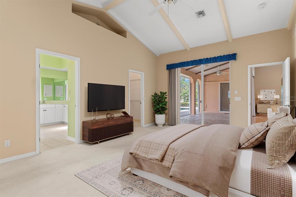 A bedroom with a vaulted ceiling, beige walls, carpeted floors, and a sliding glass door — 3825 BORDEAUX DRIVE, PUNTA GORDA, FL